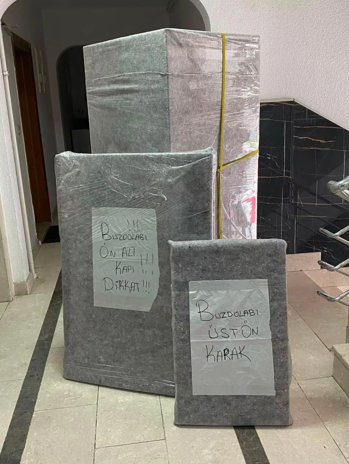 Battaniyeye sarılmış buzdolabı parçaları; üzerlerinde hangi parça olduğunu yazan el yazısı etiketler