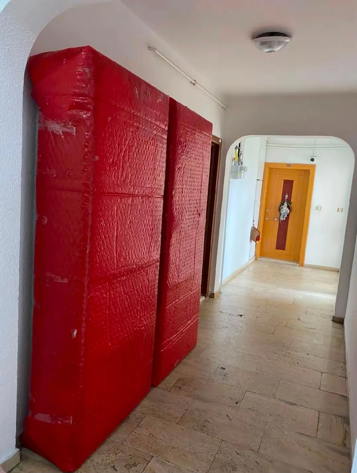 Kırmızı ambalajla sarılmış gardırop, dairenin koridorunda taşınmayı beklerken