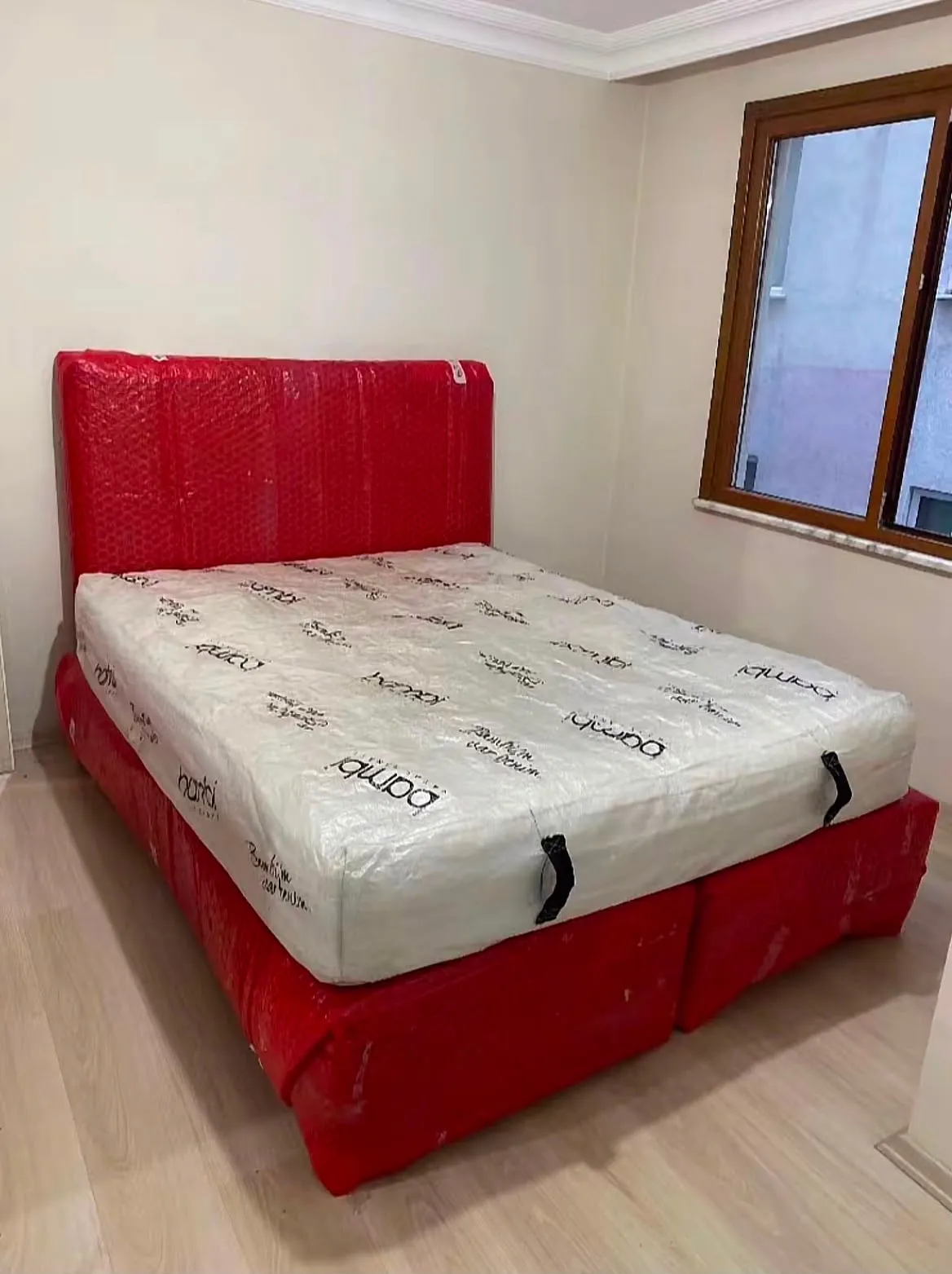 Kırmızı ambalajla sarılmış yatak bazası ve üzerinde ambalajlı şilte